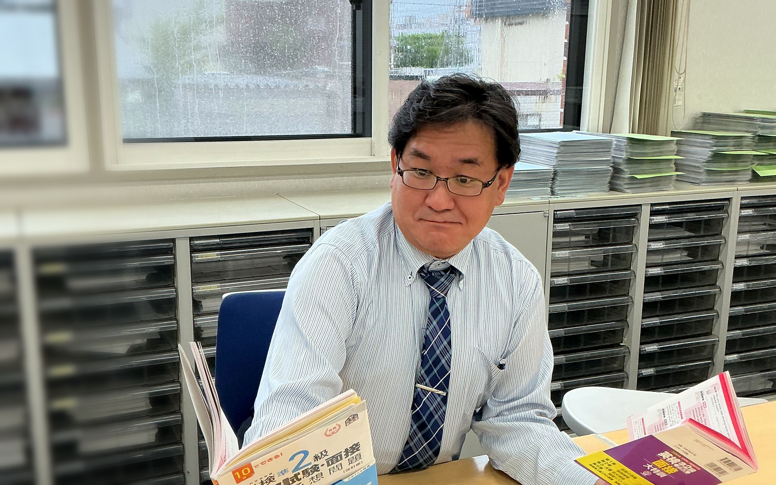 英検2級の教材を見比べながら学習法を考える木下 学先生